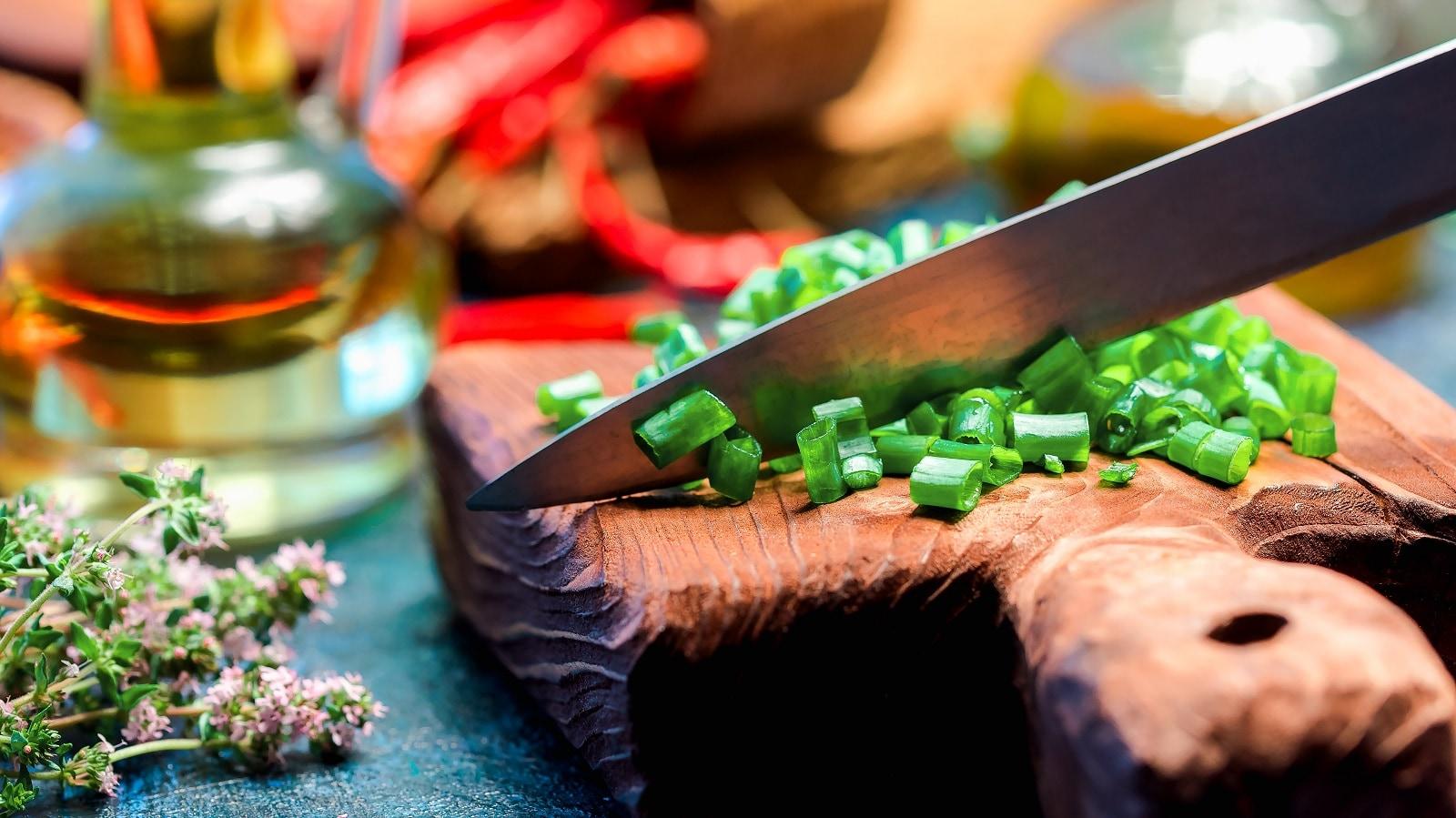 Knife poised to cut green onions on a wooden cutting board