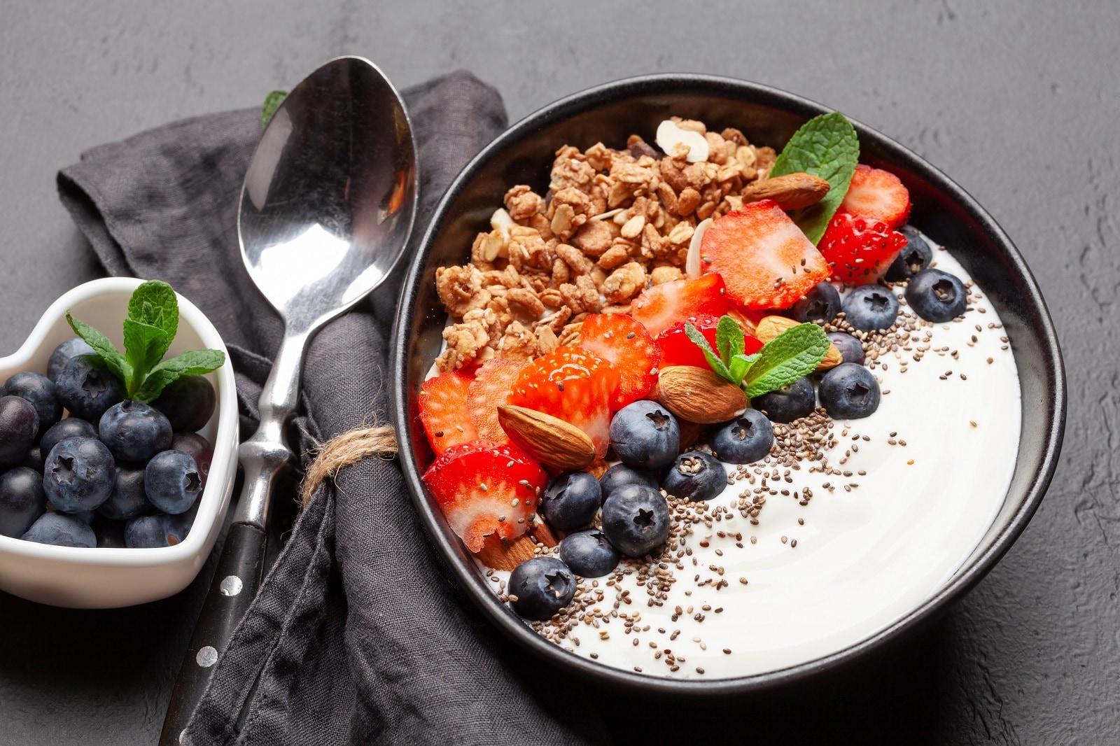 Greek yogurt bowl with blueberries, strawberries an granola, sitting beside a spoon and charcoal napkin