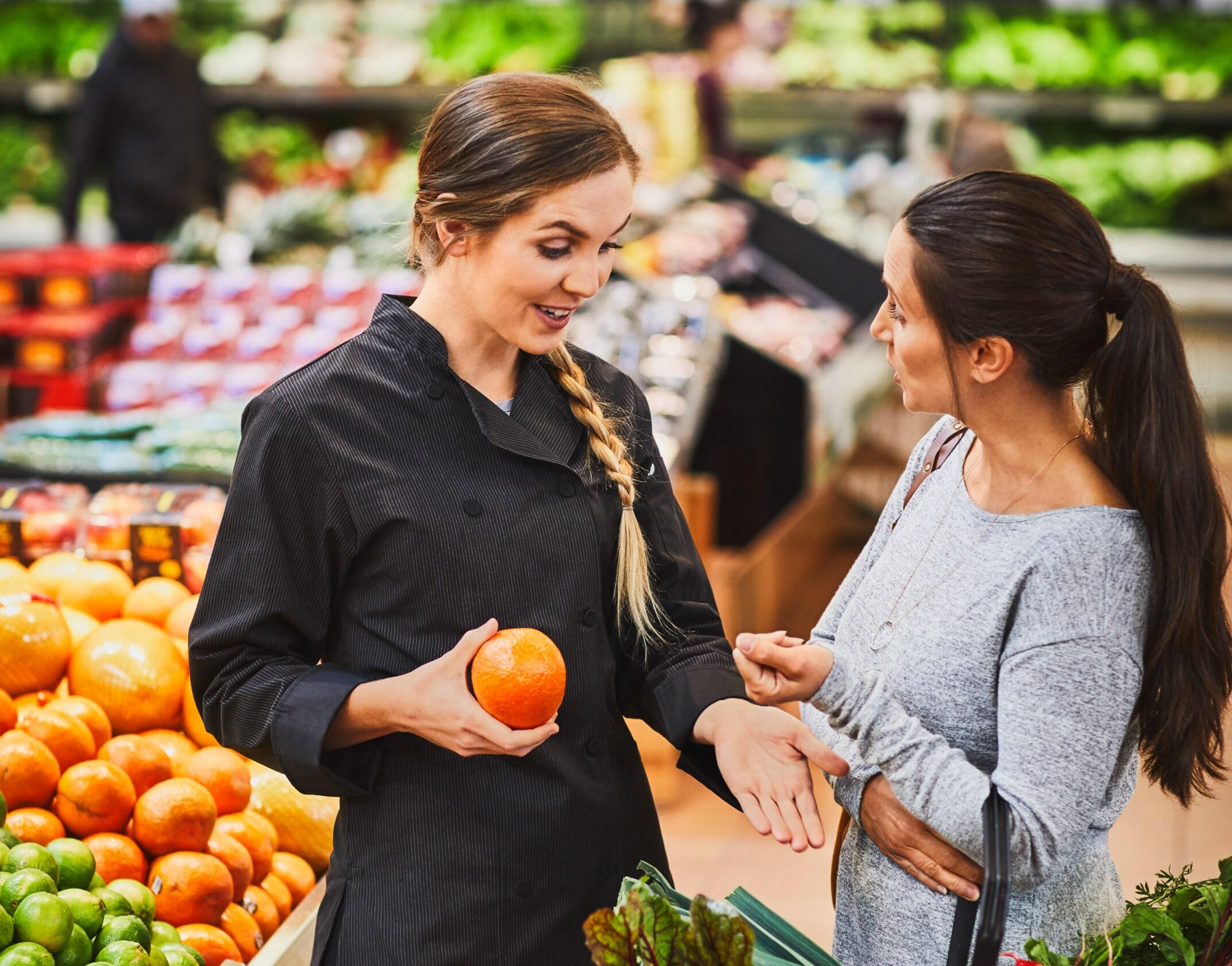 A dietitian speaking with a customer in the fruit aisle of a grocery store.