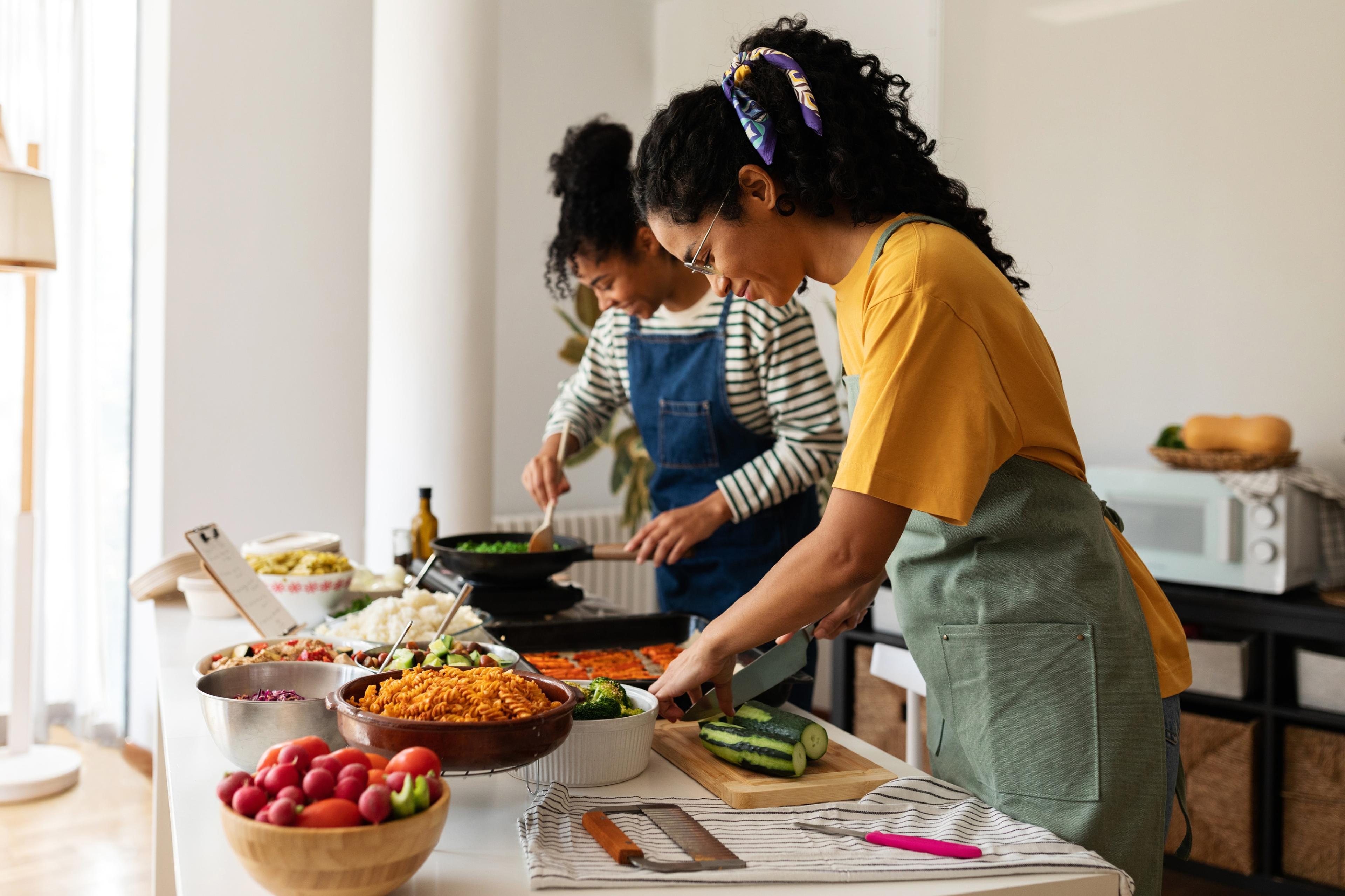 Deux femmes avec un tablier qui préparent un repas aux couleurs vives.