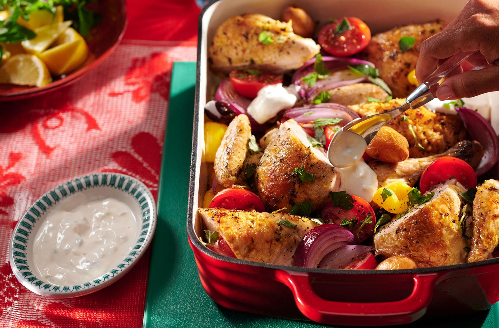 A ceramic roasting pan with with large pieces of chicken roasted with chunks of tomatoes, potatoes, onions and bell peppers.