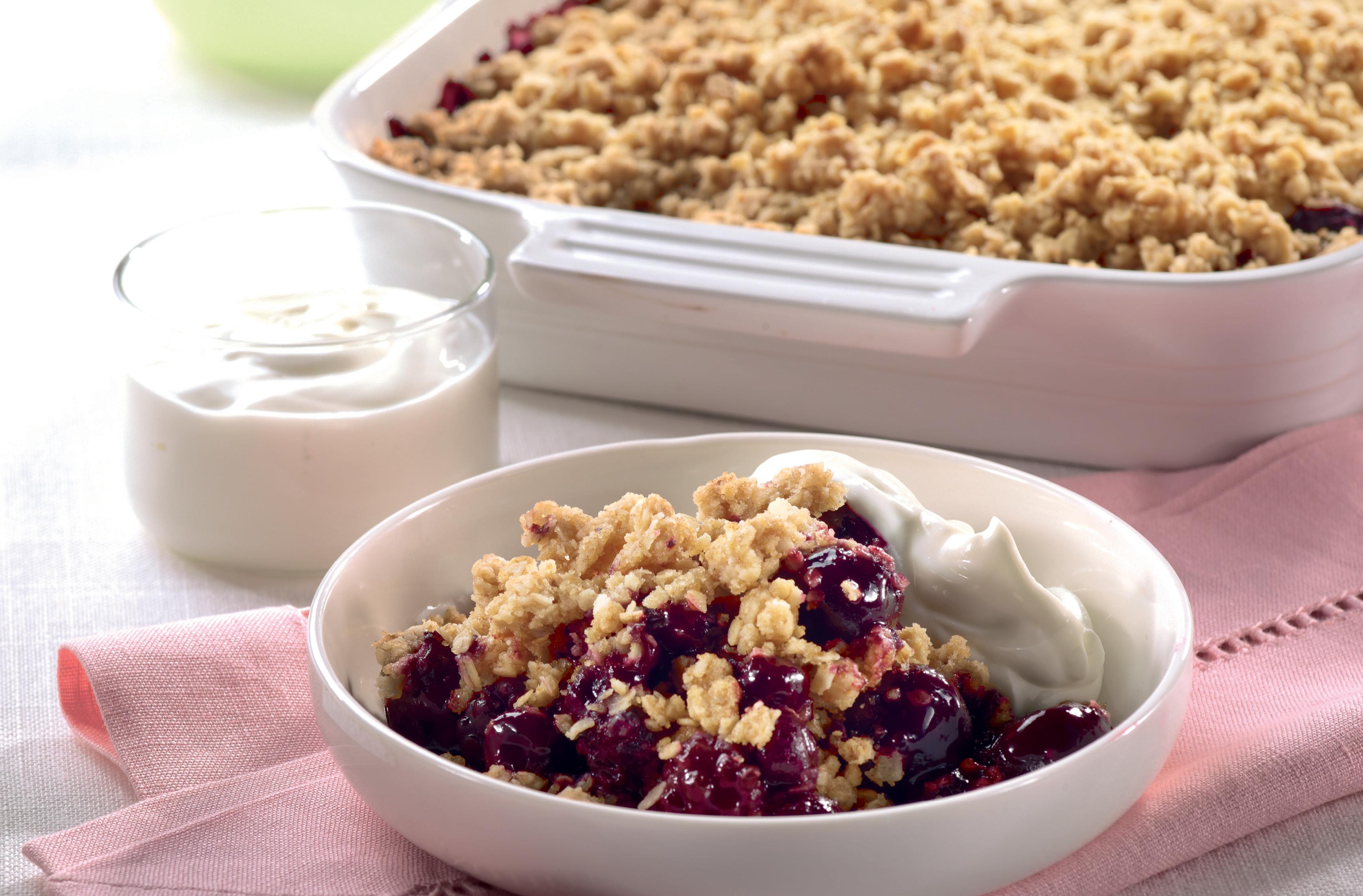 Bowl of power fruit & oat crumble with yogurt by a baking dish of crumble
