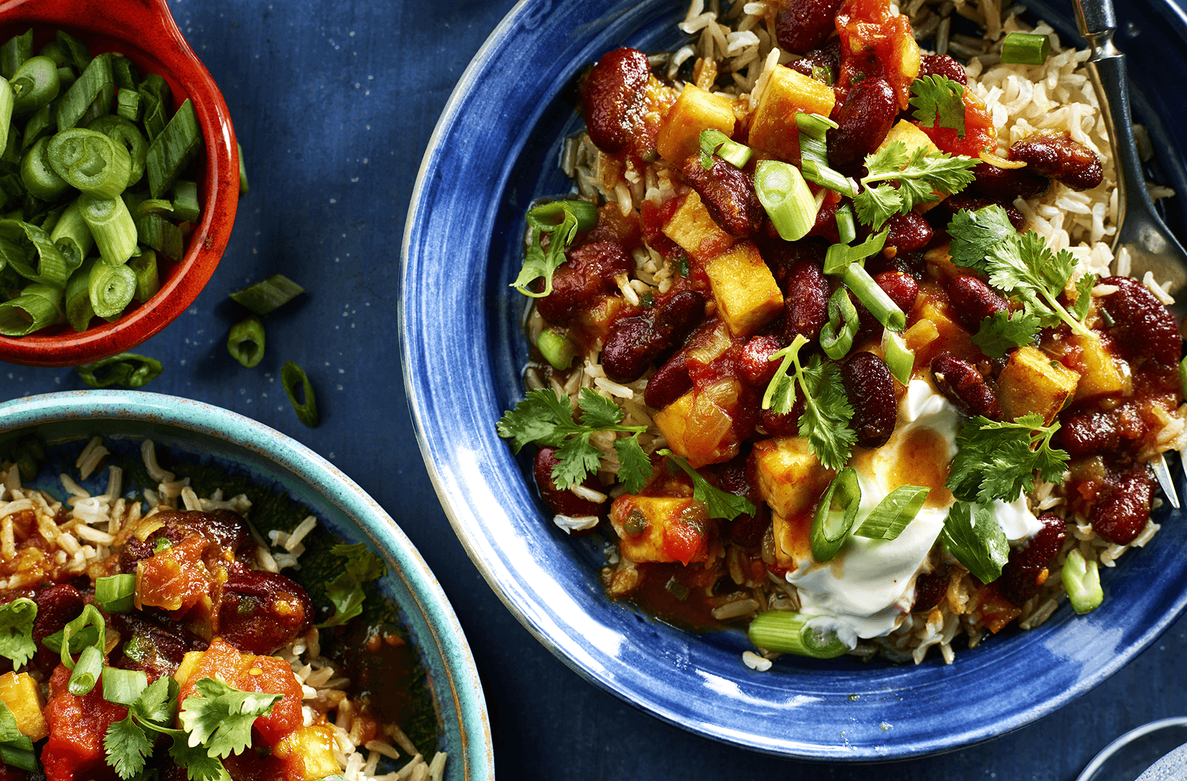 Scallion, coriander and sour cream top kidney bean curry and rice in bowls
